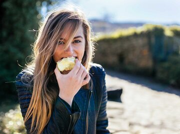 Frau steht in der Natur und isst einen Apfel. | © Getty Images / Westend61