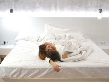 Paar liegt Arm in Arm im Bett mit weißer Bettwäsche und kuschelt. | © Getty Images / Irina Zharkova / EyeEm
