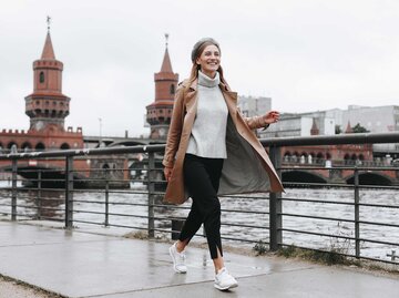 Junge Frau mit braunem Mantel läuft am Flussufer in Berlin entlang.  | © Getty Images / Mykhailo Lukashuk