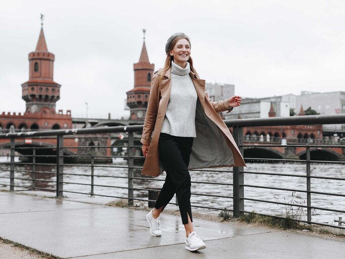 Junge Frau mit braunem Mantel läuft am Flussufer in Berlin entlang.  | © Getty Images / Mykhailo Lukashuk