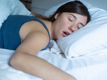 Frau liegt auf dem Bauch im Bett und schnarcht. | © Getty Images / tommaso79