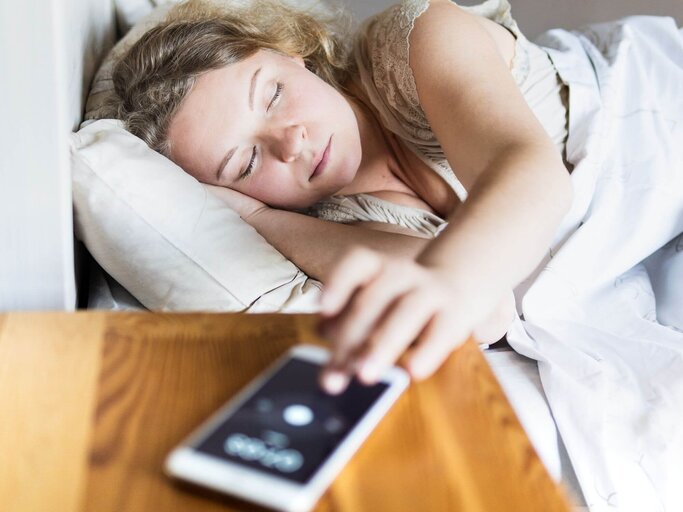 Frau im Bett drückt Snooze auf Handy | © Getty Images/leonovo