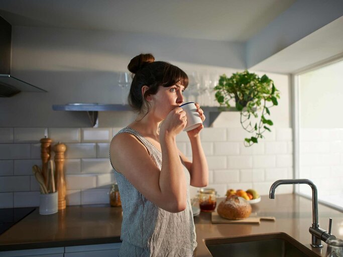 Frau trinkt aus einer Tasse und blickt aus dem Fenster | © Getty Images/Dougal Waters