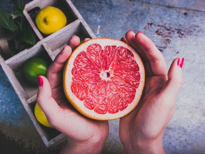 Frau hält eine aufgeschnittene Grapefruit in den Händen | © Getty Images/npdesignde