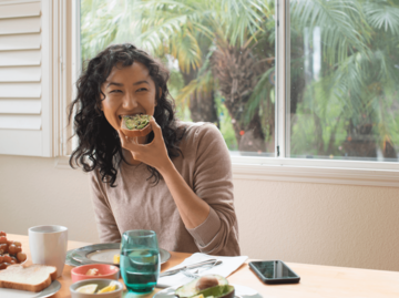 Frau isst Avocado-Toast am Frühstückstisch | © Getty Images/Eternity in an Instant