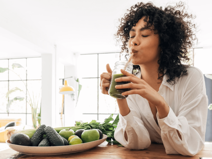 Frau trinkt grünen Smoothie am Tisch | © Getty Images/Daniel de la Hoz