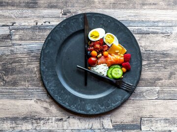 Teller mit Essen und Uhrzeigern von oben fotografiert | © Getty Images/lacaosa