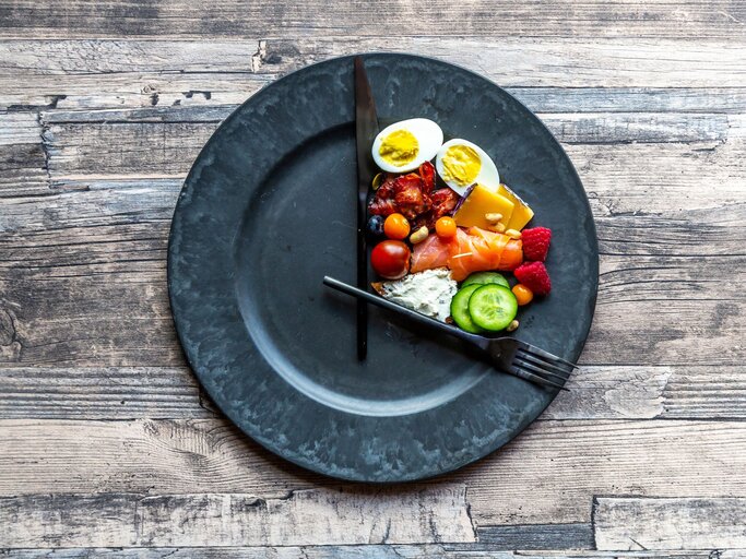 Teller mit Essen und Uhrzeigern von oben fotografiert | © Getty Images/lacaosa