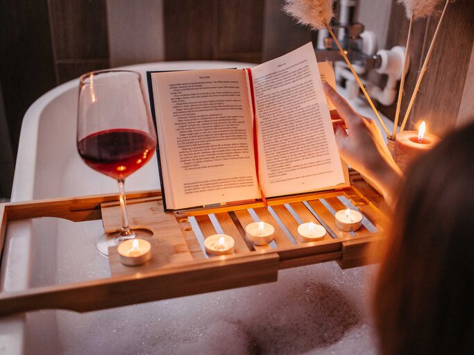 Frau sitzt in einer Badewanne, liest ein Buch und trinkt ein Glas Rotwein. | © Getty Images / Vuk Saric