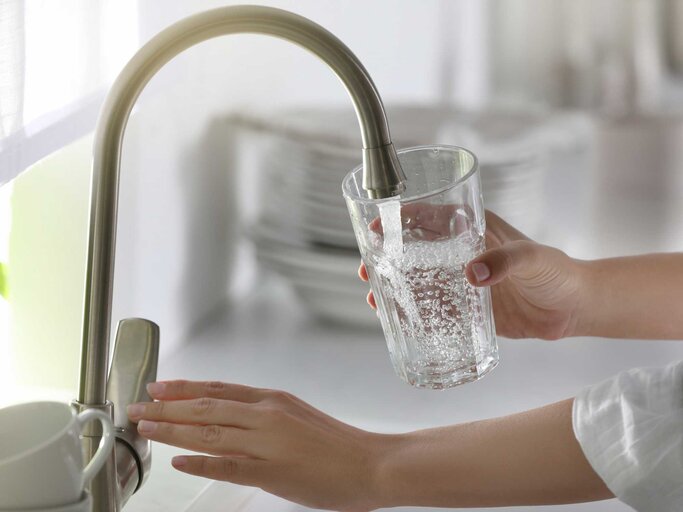 Frau gießt Wasser aus dem Wasserhahn in ein Glas | © Getty Images/Liudmila Chernetska