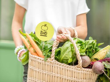 Frau hält Korb mit Gemüse und Schild, auf dem Bio steht | © Getty Images/RossHelen