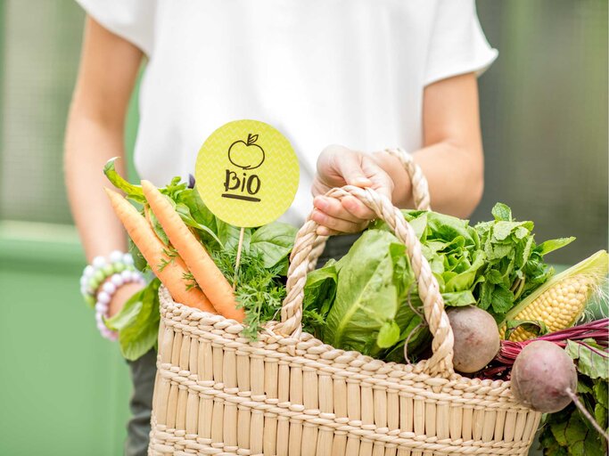 Frau hält Korb mit Gemüse und Schild, auf dem Bio steht | © Getty Images/RossHelen