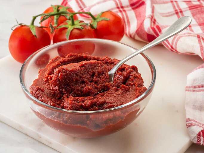 Glasschale mit Tomatenmark steht auf einer Marmorplatte. | © Getty Images / BURCU ATALAY TANKUT