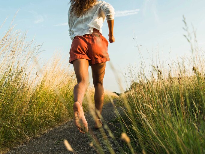 Frau läuft im Sommer barfuß durch die Wiese. | © Getty Images / Westend61