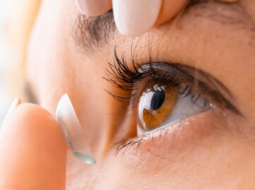 Nahaufnahme einer Frau mit braunen Augen, die sich Kontaktlinsen in die Augen legt | © Getty Images/Volodymyr Kalyniuk