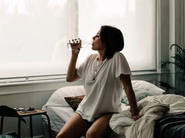 Frau sitzt im Bett und trinkt ein Glas Wasser | © Getty Images/Westend61