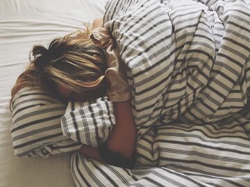 Frau schläft eingemummelt in Bett mit gestreifter Bettwäsche | © Getty Images/Marco Poggioli / EyeEm