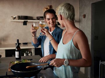 Zwei junge Frauen kochen zusammen und stoßen mit einem Glas Wein an | © Getty Images/Klaus Vedfelt