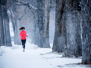 Frau joggt durch den verschneiten Wald im Winter | © Getty Images/Jordan Siemens
