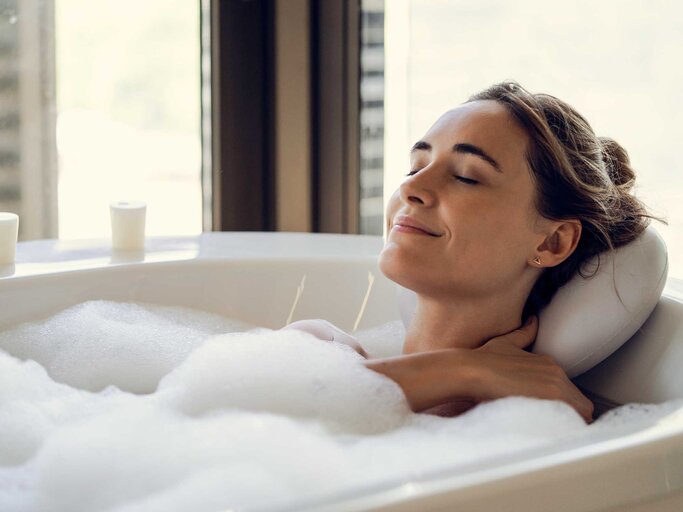 Junge Frau liegt in der Badewanne und nimmt ein Schaumbad. | © Getty Images / Frederic Cirou