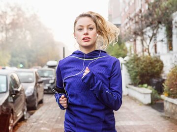 Frau in blauer Trainingsjacke joggt eine Straße entlang und schaut angestrengt. | © Getty Images / Betsie Van Der Meer