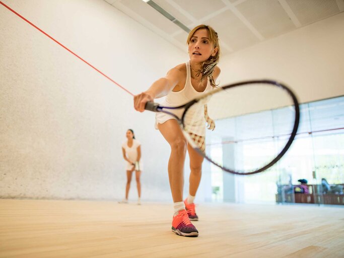 Zwei Frauen in weißer Kleidung spielen Squash in einer Halle. | © Getty Images / andresr