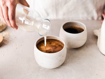 Frau schüttet Hafermilch in ihren Kaffee | © Getty IMages/alvarez