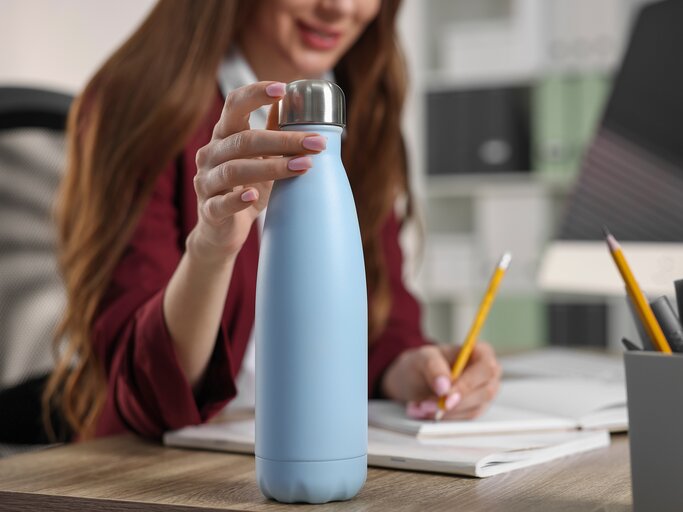 Eine junge Frau schreibt etwas und hat eine angebrochene Wasserflasche vor sich | © GettyImages/Liudmila Chernetska