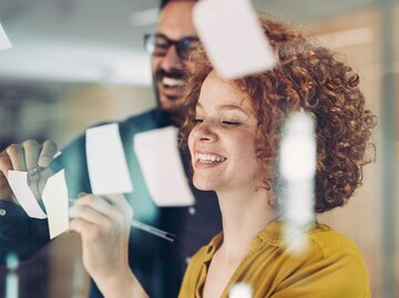 eine Frau mit lockigen roten Haaren schreibt auf eine Memo | © pixelfit