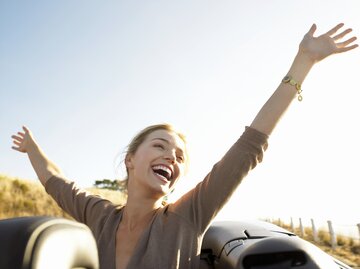 Frau sitzt mit erhobenen Armen im Cabrio und lächelt | © Getty Images/Digital Vision.