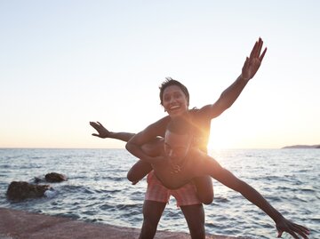 Mann trägt Frau am Strand Huckepack | © Getty Images/Klaus Vedfelt