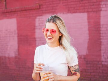 Blonde Frau trägt pinke Sonnenbrille und lacht | © Getty Images/Stephen Zeigler