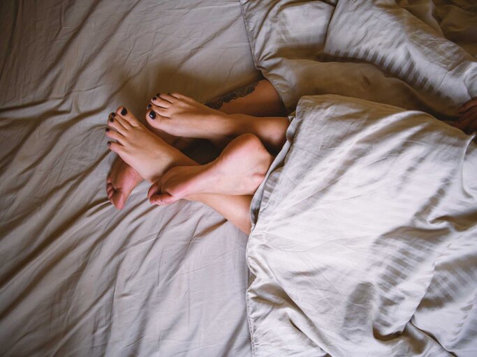 Paar liegt unter der Bettdecke, nur die Füße sind sichtbar | © Getty Images/RealPeopleGroup