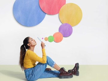 Frau sitzt auf dem Boden und pustet bunte Seifenblasen. | © Getty Images / We Are
