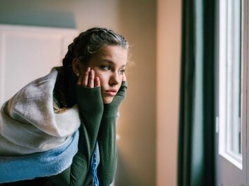 Junge Frau, die am Bett sitzt und durch das Fenster schaut | © Getty Images/martin-dm
