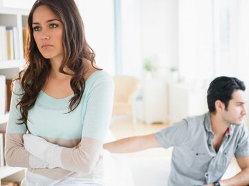 Frau steht mit dem Rücken zu ihrem Partner, während er auf der Couch sitzt | © Getty Images/	JGI/Jamie Grill