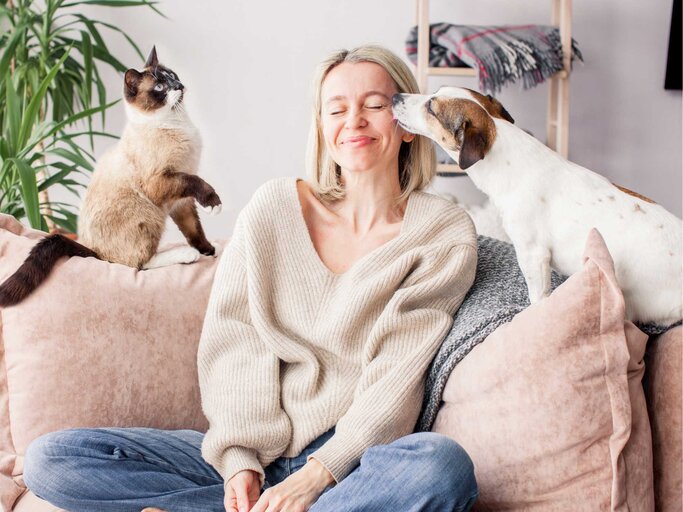 Frau sitzt auf dem Sofa mit Katze und Hund | © Getty Images/TatyanaGl