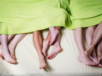 Mehrere Füße nebeneinander und ineinander verschlungen auf einem Bett | © GettyImages/Bilyana Stoyanovska/EyeEm