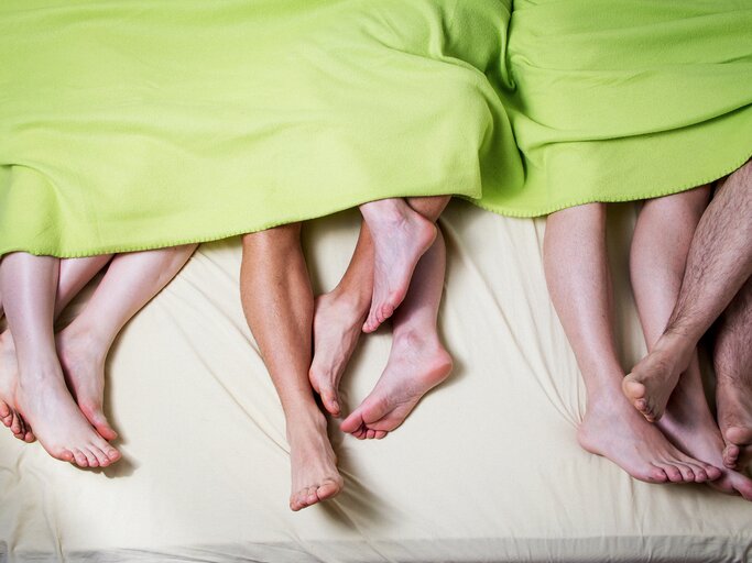 Mehrere Füße nebeneinander und ineinander verschlungen auf einem Bett | © GettyImages/Bilyana Stoyanovska/EyeEm