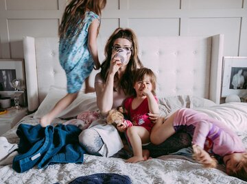 Frau sitzt auf dem Bett, während ihre Töchter um sie herum sitzen und laufen | © Getty Images/Davin G Photography