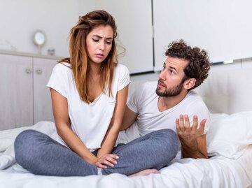 Frau sitzt frustriert auf dem Bett, während ihr Partner auf sie einredet | © Getty Images/stefanamer