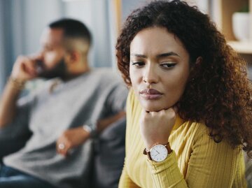 Frau sitzt nachdenklich und abgewandt von ihrem Partner auf der Couch  | © Getty Images/Delmaine Donson