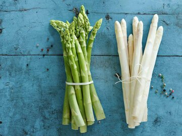 Ein Bund grüner und ein Bund weißer Spargel auf blauem Untergrund | © Getty Images/Westend61