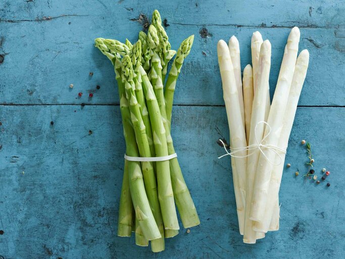 Ein Bund grüner und ein Bund weißer Spargel auf blauem Untergrund | © Getty Images/Westend61