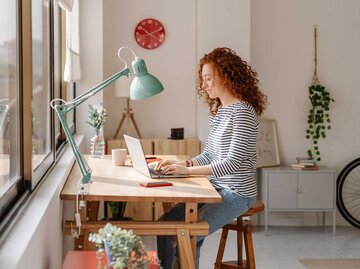 Frau sitzt am Schreibtisch in ihrer Wohnung und arbeitet am Laptop.  | © Getty Images / COROIMAGE