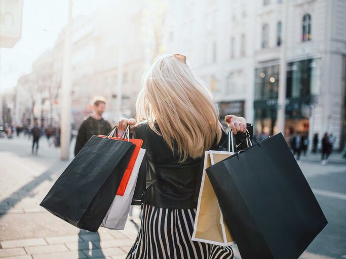Blonde Frau von hinten mit zahlreichen Einkaufstüten über der Schulter | © Getty Images/ReMa
