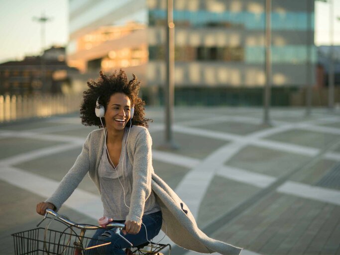 Gut gelaunte Frau mit Kopfhörern auf einem Fahrrad | © Getty Images/MStudioImages