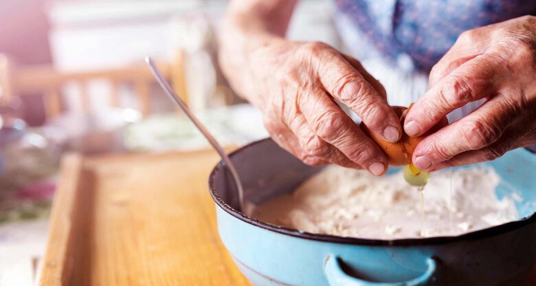 Ältere Frau backt und gibt ein Ei in eine Schüssel | © Getty Images/Halfpoint