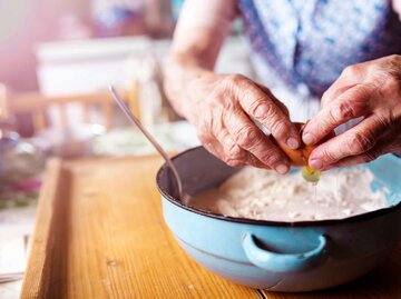 Ältere Frau backt und gibt ein Ei in eine Schüssel | © Getty Images/Halfpoint