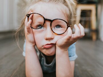 Kind liegt auf Boden und stützt Kopf mit schräger Brille auf | © Getty Images/Catherine Falls Commercial